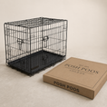 Load image into Gallery viewer, A black metal wire pet crate with a black plastic tray sits next to a brown cardboard box printed with the brand name 'POSH POOS LONDON' on a warm beige studio background.