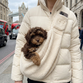 Load image into Gallery viewer, A person wearing a cream puffer jacket carries a small brown curly-haired dog in a cream fleece dog sling bag, with London street and Tower Bridge visible in the background.