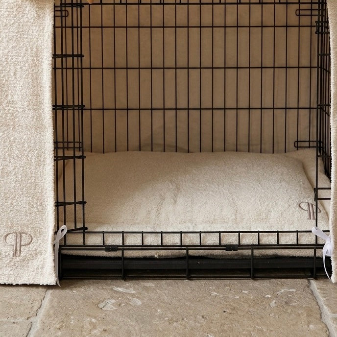 A black metal wire dog crate with a soft cream-colored boucle mattress inside with embroidered Posh Poos PP monogram.