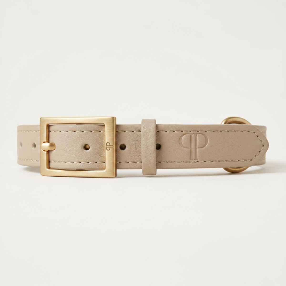 A beige leather puppy collar with a gold-tone metal buckle, shown against a clean off-white background. The embossed logo on the belt strap belongs to the brand Posh Poos.
