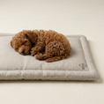 Load image into Gallery viewer, A small brown curly-haired dog is sleeping curled up on a rectangular striped dog crate mattress bed with a stitched monogram logo in the corner, photographed on a plain light beige background.
